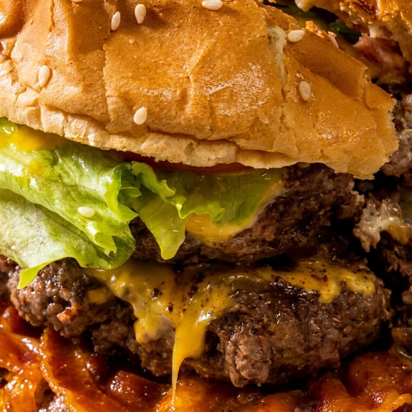 Close-up of a double cheeseburger with melted cheese, lettuce, and bacon on a sesame seed bun.