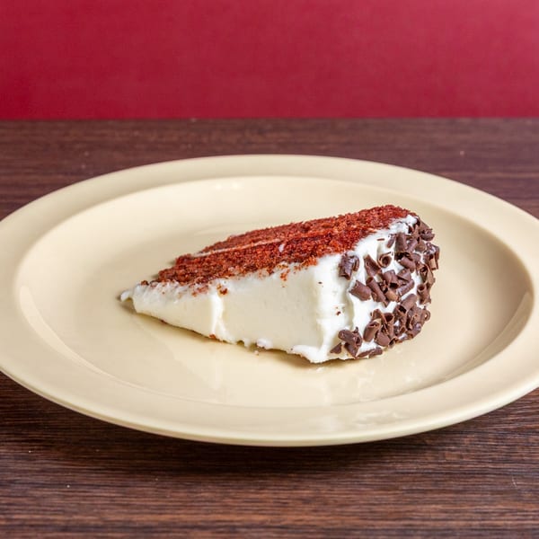 Slice of creamy white cake topped with reddish spice and chocolate shavings on a beige plate.