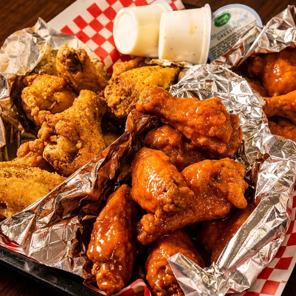 A basket of crispy fried chicken wings and saucy buffalo wings with ranch dressing cups.