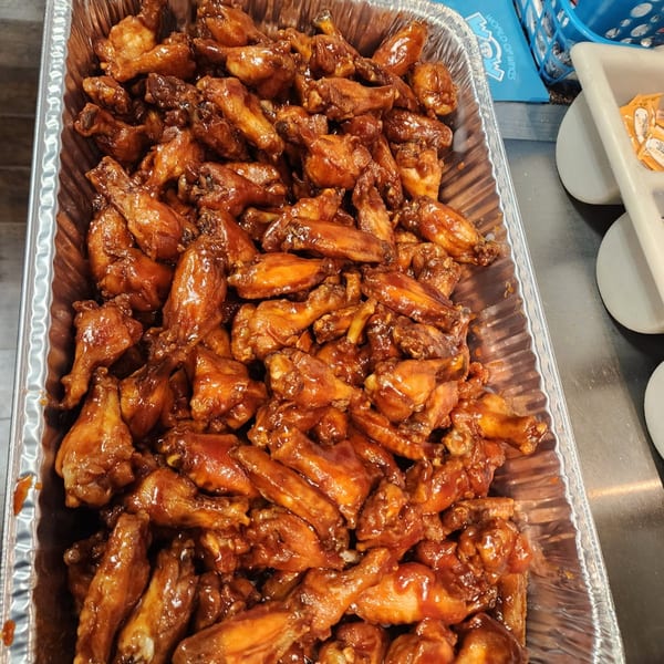 A large foil pan filled with numerous glazed chicken wings, ready for serving.