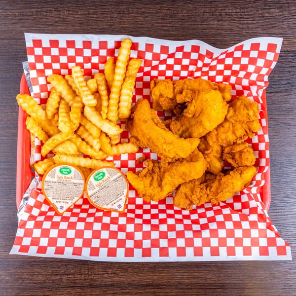 Basket of crispy fried chicken tenders and crinkle-cut fries with ranch dipping cups on red-and-white checkered paper.