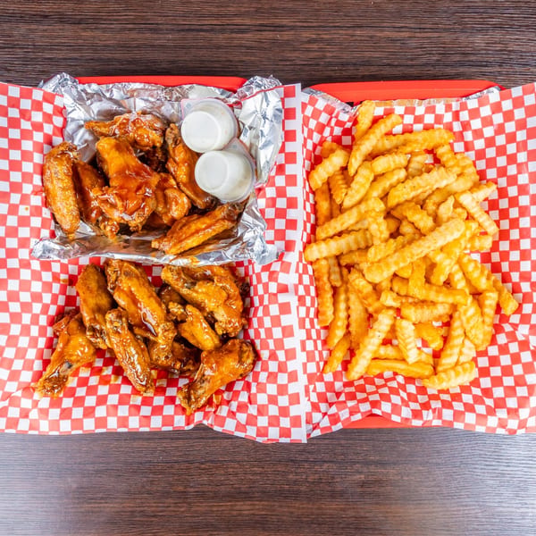 Two trays of saucy chicken wings and crinkle-cut fries served on red-and-white checkered paper.