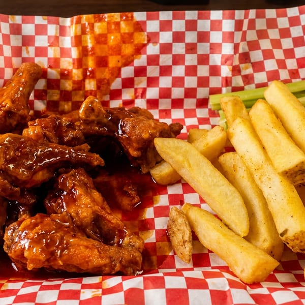 A red tray holds buffalo wings and french fries on red and white checkered paper.